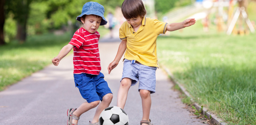 Children kicking a soccer ball on the side walk