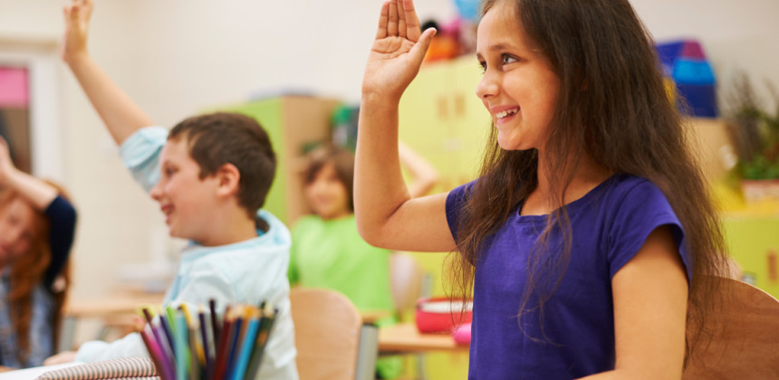 Young girl sitting in class with her hand up