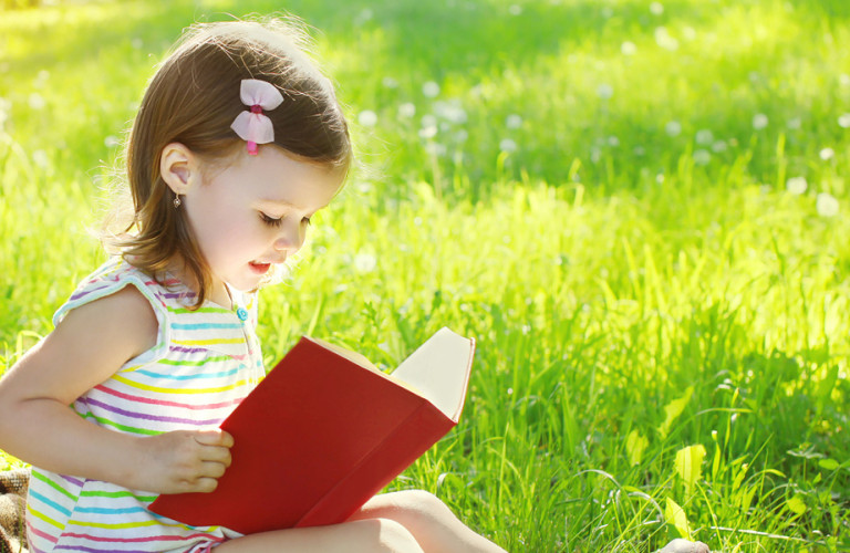 Little girl reading outside in the grass