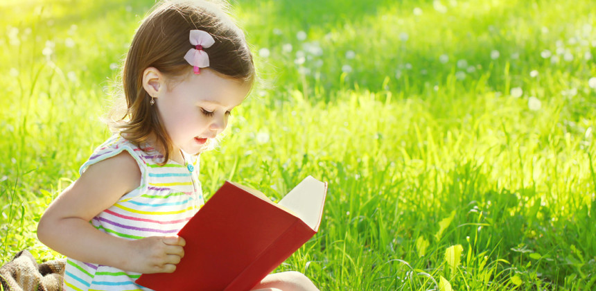Little girl reading outside in the grass