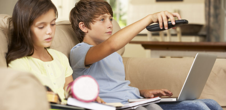 Two Children Distracted By Television Whilst trying To Do With Homework