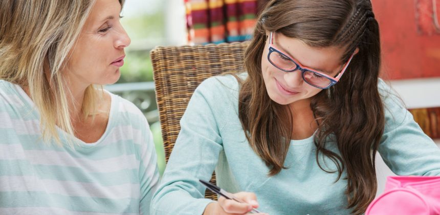 Mother and teen daughter sitting together while daughter writes in notebook