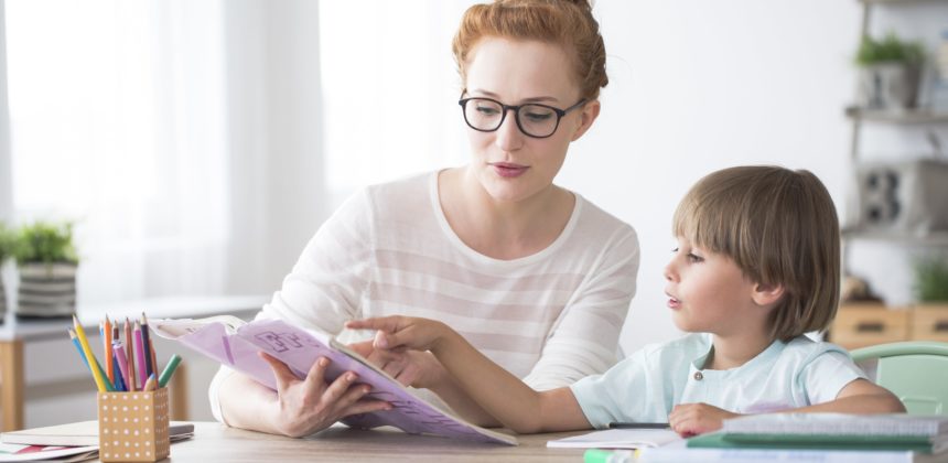 Female tutor reading with a child at a desk.