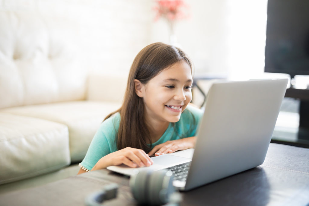 Happy, smiling child sitting in front of a couch at a laptop getting homework help online
