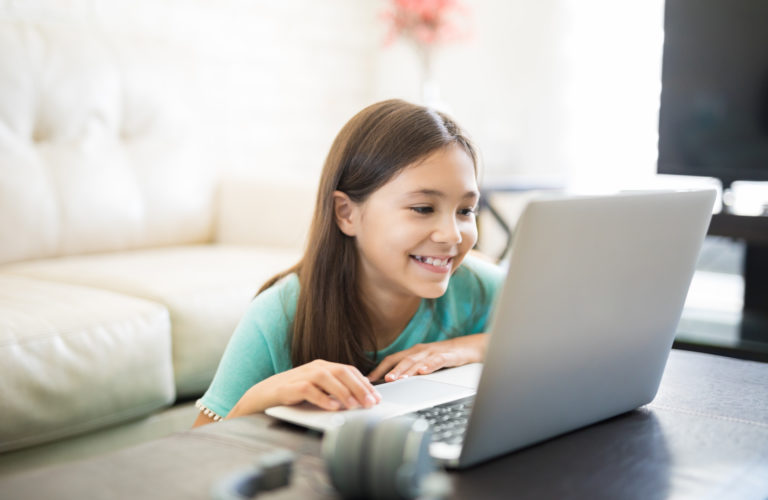 Happy, smiling female student sitting in living room at a laptop getting homework help online