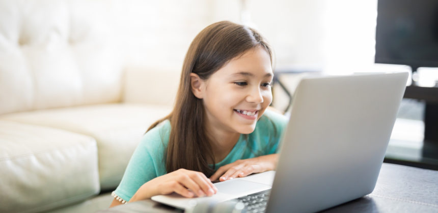Happy, smiling female student sitting in living room at a laptop getting homework help online