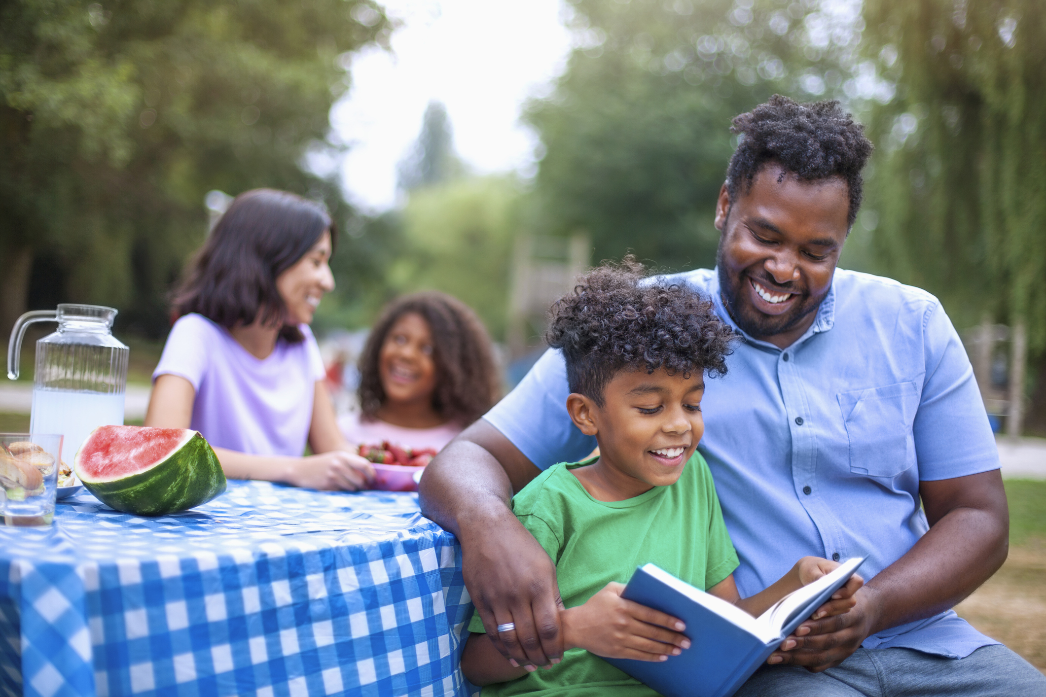 Son reading book with his African-American father at family outdoor picnic
